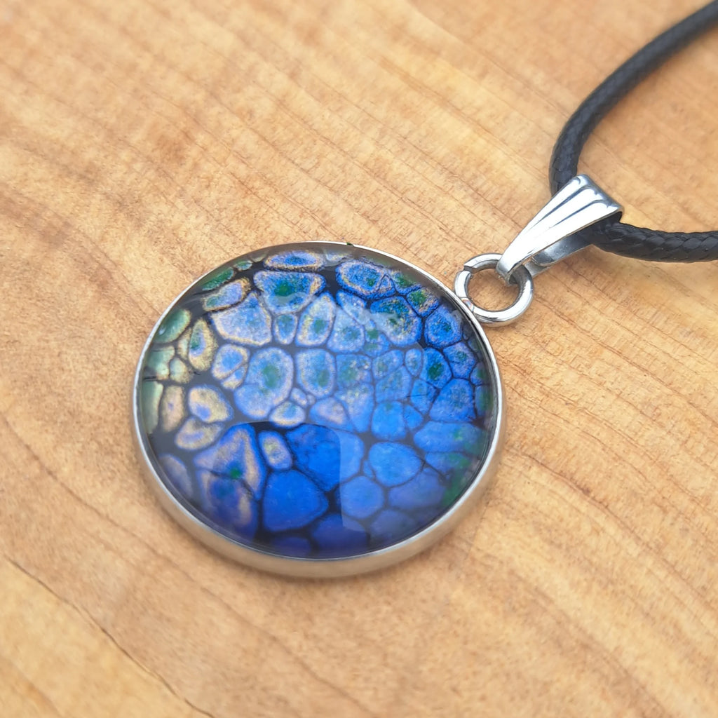 Stunning deep blue pendant with dragon scale pattern in emerald & gold. 20mm stainless steel on 18" cord.
