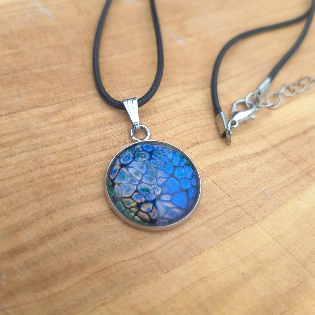 Stunning deep blue pendant with dragon scale pattern in emerald & gold. 20mm stainless steel on 18" cord.