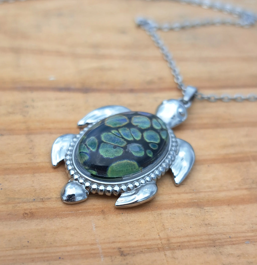 Turtle-shaped pendant with green and black pattern on a wooden surface