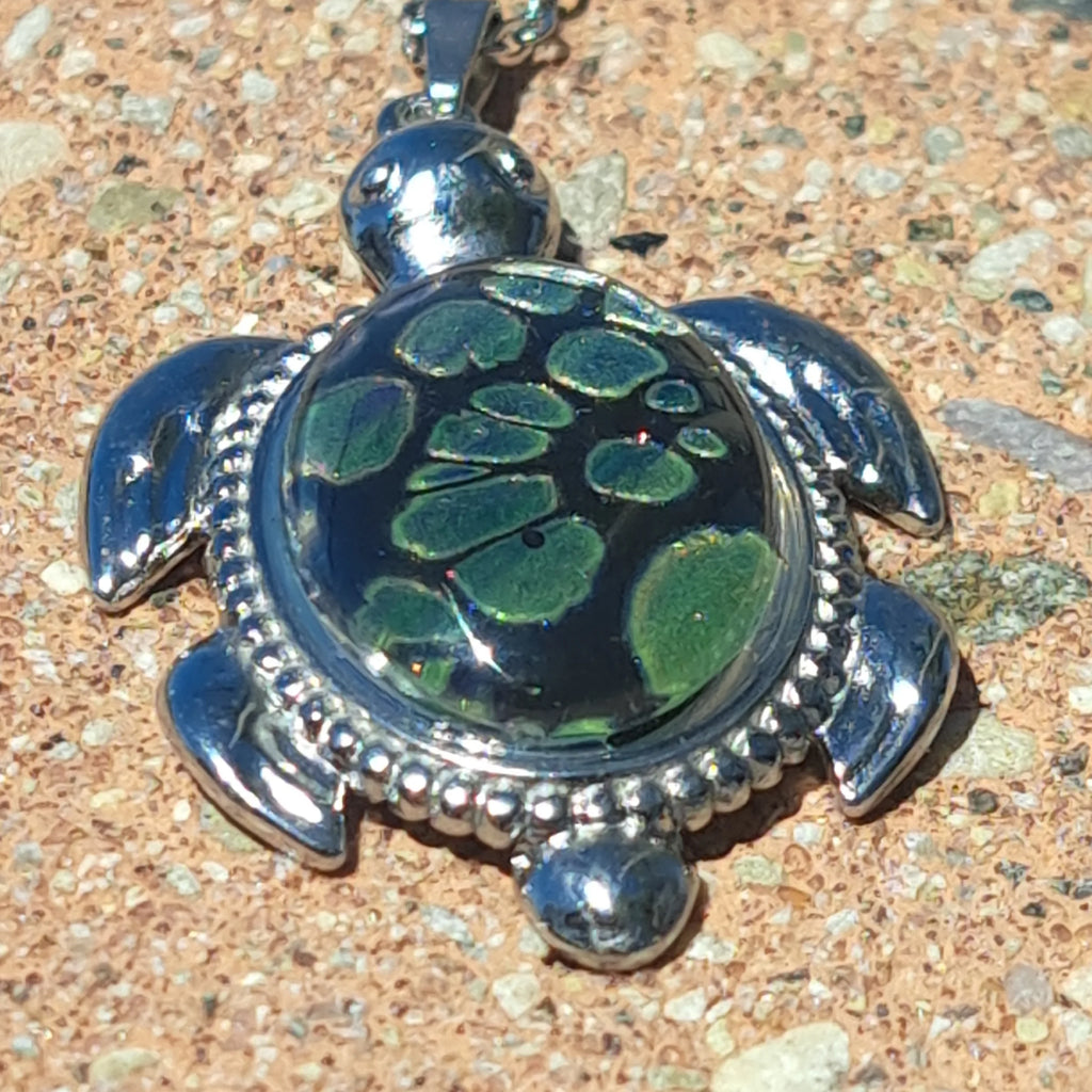 Turtle-shaped pendant with green stone on a textured surface